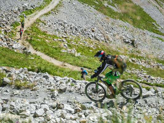 Adventure sports photography - rider conquering an uneven mountain path with loose gravel and exposed tree roots